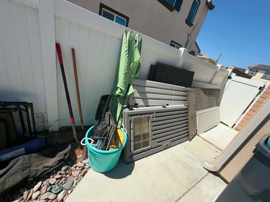 Patio umbrella, shed panels, a headboard, and yard tools staged for pickup on a Riverside County cleanout